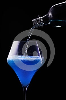 Blue drink is poured into a glass. Black background