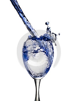 A blue drink is poured into wine glass causing a splash, isolated on white background