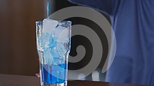 Blue drink pours into glass. Glass with ice and cocktail. Exotic beverage at the bar. Slow motion.