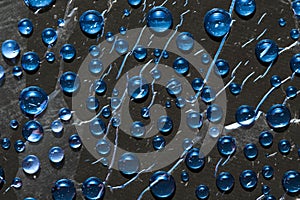 Blue drops of water flow down on black surface.