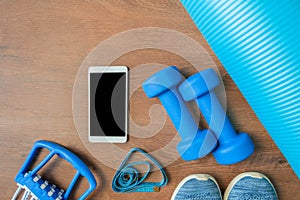 Blue dumbbells and chesty expanders, measure tape, sneakers, phone, and yoga mat. Fitness concept photo