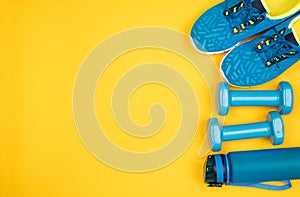Blue dumbbells, trainers and a water bottle on yellow background