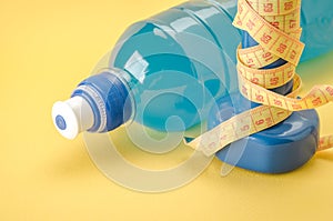 Blue dumbbells with yellow centimeter and bottle/blue dumbbells with centimeter and bottle on a yellow background. Close up