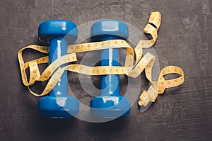 Blue dumbbells and yellow centimeter/ fitness concept with blue dumbbells and yellow centimeter on a dark background. Top view