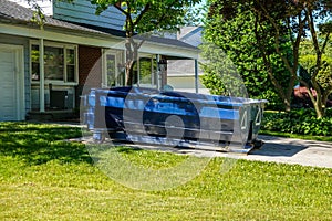 A blue dumpster in the driveway of a house in a residential neighborhood