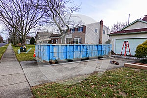 Blue dumpster in the driveway of a residential home that is undergoing renovation.