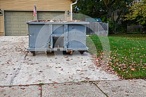 A blue dumpster filled with construction debris in the driveway of a yellow house in front of the garage doors