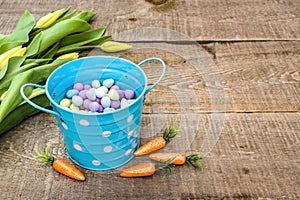 Blue easter bucket filled with candy eggs on rustic wood plank s