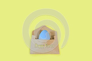 Blue easter egg in a craft envelope on a pastel yellow background, with the inscription happy easter. Happy Holiday message,