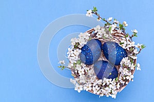 Blue easter eggs in a basket with flowers on a blue background. Horizontal photograph. Top view