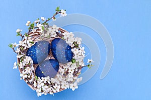 Blue easter eggs in a basket with flowers on a blue background. Horizontal photograph. Top view