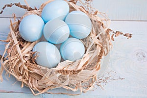 Blue Easter eggs in nest on wooden background.