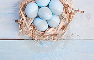 Blue Easter eggs in nest on wooden background.