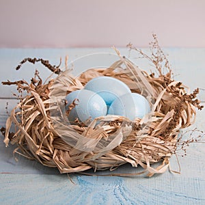 Blue Easter eggs in nest on wooden background.