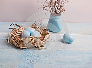 Blue Easter eggs in nest on wooden background.