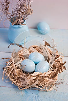 Blue Easter eggs in nest on wooden background.