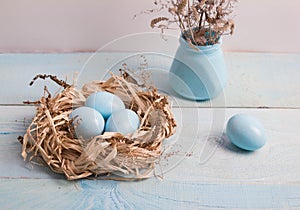 Blue Easter eggs in nest on wooden background.