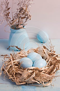 Blue Easter eggs in nest on wooden background.