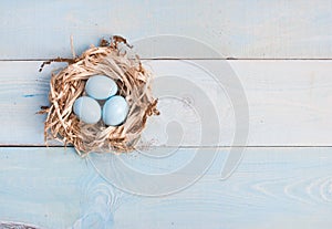 Blue Easter eggs in nest on wooden background.