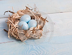 Blue Easter eggs in nest on wooden background.