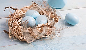 Blue Easter eggs in nest on wooden background.