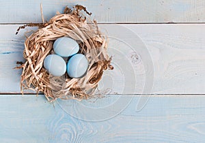 Blue Easter eggs in nest on wooden background.