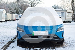 Blue electric car with green numberplate stripe with snow on the bonnet