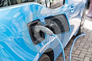 Blue electric car recharging on street with charge cable and plug leading to charge point.