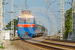 Blue electric locomotive with passenger cars turn passing rail road through the city at speed motion sunny day