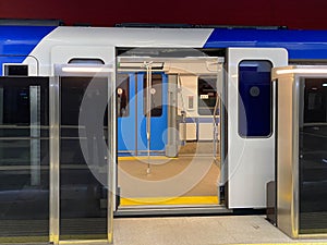 A blue electric train carriage with an open sliding mechanical door at a train station platform