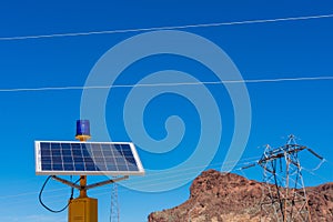 Blue emergency light fixture powered by solar panel. Blurred transmission tower background