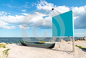 Blue empty billboard next to a local, wooden fishing boat, on the sand, at shore of the Black Sea Marea Neagra, Romanian coast. photo