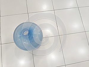 A blue, empty plastic water bottle gallon jug on a white tiled floor.