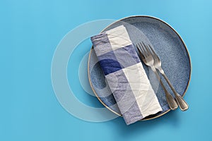 Blue empty plate, checkered napkin and forks on pastel blue background. Top view, flat lay, copy space