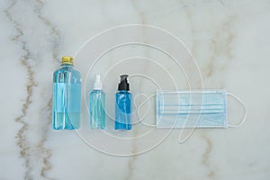 Blue Ethyl Alcohol spray bottle, Alcohol gel bottle, Alcohol in plastic bottle and blue surgical masks on the marble desk.