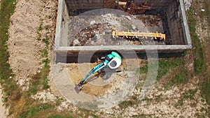 Blue excavator digs the earth with a building. bird`s eye view.