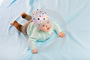 Blue-eyed baby in hat crawling