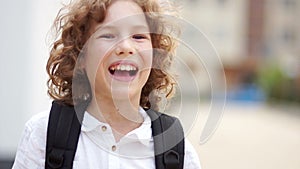 The blue-eyed boy corrects the harnesses of the backpack on his shoulder and throws back curly hair. Close up portrait