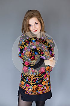 Blue eyed girl in black miniskirt wrapping herself in warm multicoloured ethnic style jacket