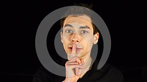Blue-eyed man making a silence gesture, black background