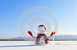 The blue eyed smiling snowman in red hat, gloves and plaid scarf holds the icicle in hand. Joyful cold winter morning.