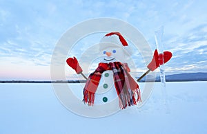 The blue eyed smiling snowman in red hat, gloves and plaid scarf holds the icicle in hand. Joyful cold winter morning.