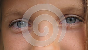 Blue eyes of beautiful small girl blinking and looking into camera with a sad sight. Portrait of cute face of young