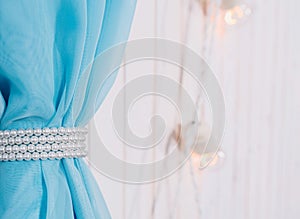 Blue fabric on a white wooden background in selective focus. The curtain is decorated with white pearls. In the background, electr photo