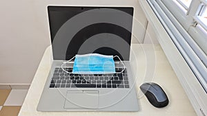 Blue face protection mask on a laptop near a mouse