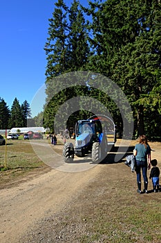 Blue farm tractor with big green trees on a dirt road with blue sky