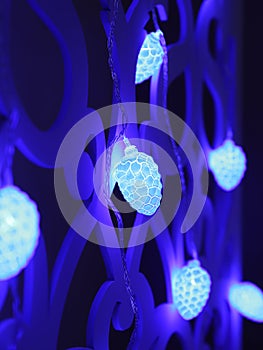 Blue fir cones Christmas lights garland on dark background. Christmas or new year led lights garland. Blurred glowing light bulb