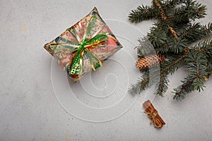 Blue fir tree branch with big cone, wrapped present box and cinnamon sticks on white wooden background. Christmas blank card, copy