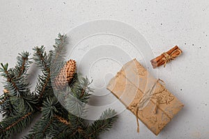 Blue fir tree branch with big cone, wrapped present box and cinnamon sticks on white wooden background. Christmas blank card, copy