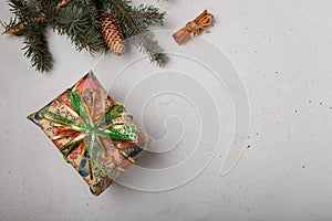 Blue fir tree branch with big cone, wrapped present box and cinnamon sticks on white wooden background. Christmas blank card, copy